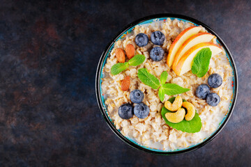 Oatmeal with blueberry, almonds and cashew nuts on a dark background. Oatmeal porridge bowl with apples and mint leaves. Top view. Copy space - obrazy, fototapety, plakaty