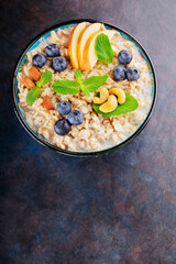 Oatmeal with blueberry, almonds and cashew nuts on a dark background. Oatmeal porridge bowl with apples and mint leaves. Top view. Copy space