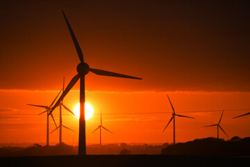 Deep orange sunset falls behind a field of giant wind turbines