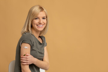 Coronavirus vaccination advertisement. Happy vaccinated lady showing arm with plaster after covid-19 vaccine injection - obrazy, fototapety, plakaty