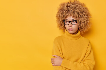 Horizontal shot of thoughtful curly haired young woman keeps arms folded concentrated away...
