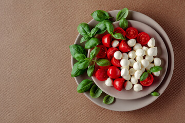 Caprese salad with tomato, mini mozzarella and basil on a brown background.