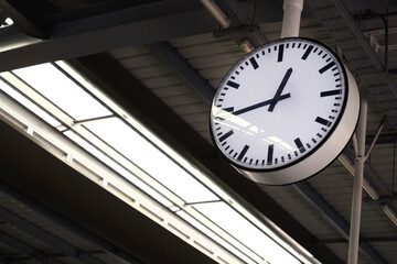 a modern style train station's hanging clock show about quarter to 1 pm in the evening day time