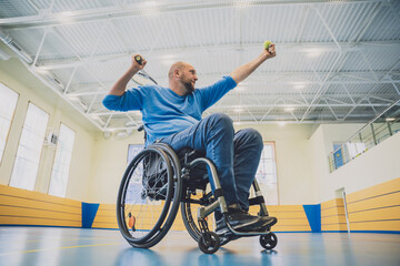 Fototapeta na wymiar Adult man with a physical disability who uses wheelchair playing tennis on indoor tennis court