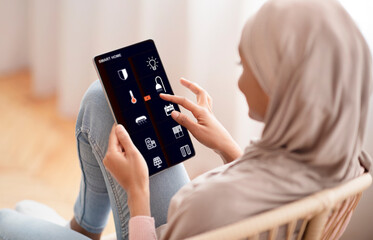 Woman controlling smart home devices using digital tablet with launched app in living room