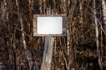 Close up of a white blank sign on a wood post next to a forest with copy space