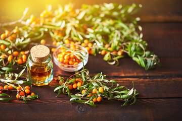 Glass bottle with sea buckthorn oil berries and sea buckthorn branches on wooden background