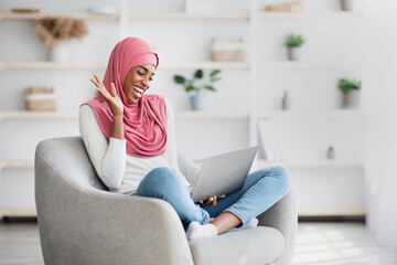 Distant Communication. Cheerful black woman in hijab making video call on laptop