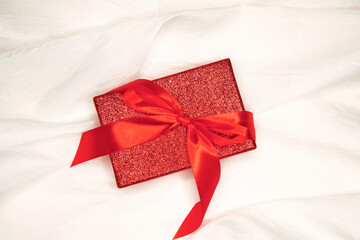 Red gift box with red bow on the white silk background. Valentine day concept