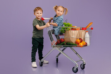 Little boy pushing a little girl inside a shopping cart. Isolated concept image..