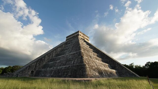 Timelapse of the temple of Kukulcan (El Castillo) on the green loan, the center of the archeological site in Chichen Itza, a city built by the Maya people. Clouds float above the temple. No tourists