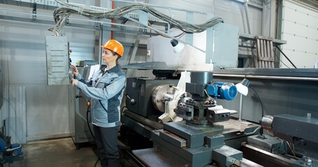 A woman worker operates a lathe for drilling components. Factory for the production of metal lathes