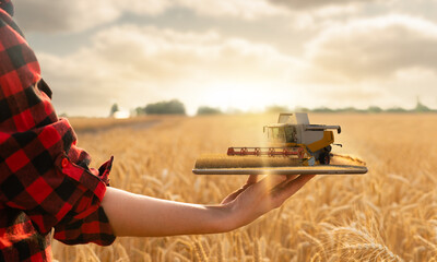 Farmer holding a tablet with a combine harvester. Digital transformation in agriculture. Smart farming concept