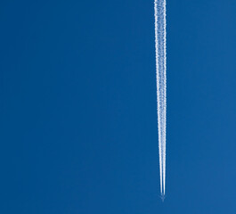 Distant passenger jet plane flying on high altitude on clear blue sky leaving white smoke trace of contrail behind. Air transportation concept.