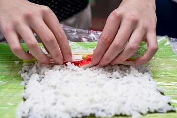 Obraz na płótnie Canvas A girl arranges chopped crab sticks on a nori leaf with rice.