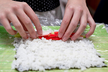 A girl arranges chopped crab sticks on a nori leaf with rice.