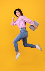 Happy armenian woman jumping or running with laptop computer in hand, having fun on yellow studio background