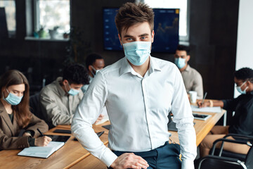 Young businessman in mask sitting on desk and posing