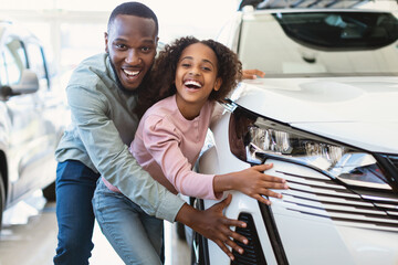 Happy black father and his cute daughter selecting new car, buying or renting automobile at auto dealership