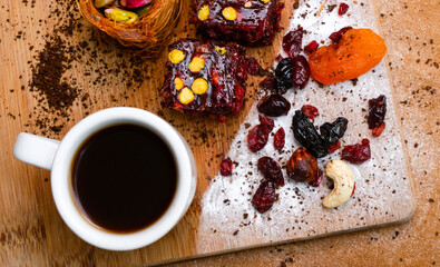 Cup with coffee next to dried fruits baklava and Turkish delight with pistachios, top view. Wooden board 
