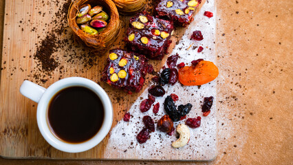 Cup with coffee next to dried fruits baklava and Turkish delight with pistachios, top view. Wooden board and free space for text