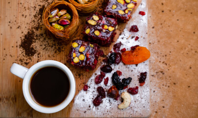 Cup with coffee next to dried fruits baklava and Turkish delight with pistachios, top view. Wooden board and free space for text
