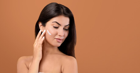 Fototapeta premium Beauty day concept. Portrait of pretty armenian woman with cream on cheek posing over brown background, panorama