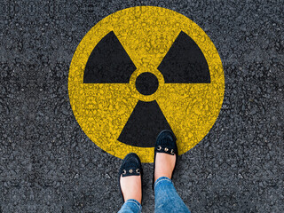 legs in shoes standing on asphalt road and radioactive sign

