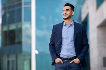 Handsome middle-eastern businessman posing by office center, panorama