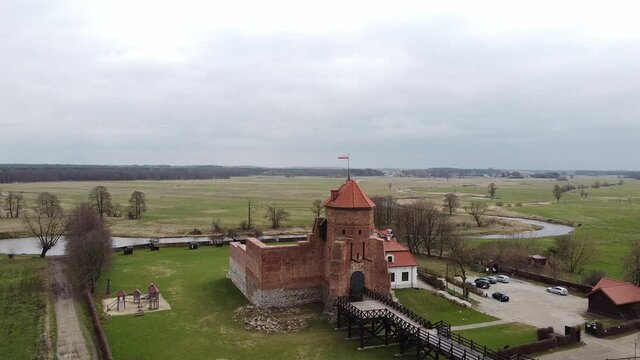 Aerial view of brick old tower with flag. Behind the tower there is a river. Place for historical tourism. Aerial View of Liw Castle in Poland.