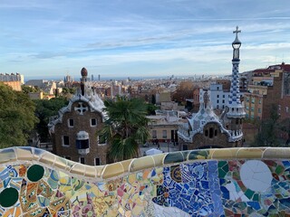 Famous colourful ceramic tiles benches at Park Guell. Panoramic view of the entrance. Skyline of Barcelona in the background. Unesco world heritage. Barcelona, Catalonia, Spain 