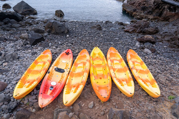 Several colorful kayak lifted on the shore between rocks in Madeira island.