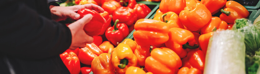 man hand holding sweet red pepper in grocery store in supermarket