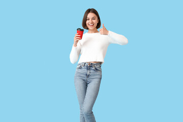 Beautiful woman with cup of coffee showing thumb-up on color background