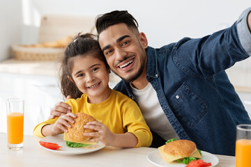 Happy Arab Dad Taking Selfie With Little Daughter While Having Lunch Together