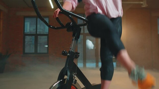 Athletic girl training on spin stationary bike riding in gym with smoke. Fit woman performs aerobic endurance training workout cardio routine on the simulators, cycle training on exercise bike indoors
