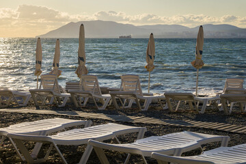 A deserted sea beach, empty sun loungers and sun umbrellas rolled up.