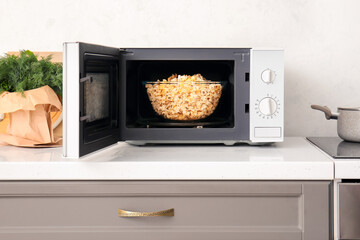Modern microwave oven with bowl of popcorn on counter near light wall - obrazy, fototapety, plakaty