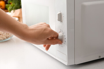 Woman adjusting white microwave oven on counter in kitchen