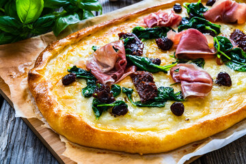 Pizza with prosciutto di Parma, spinach, sun-dried tomatoes, mozzarella and black olives on wooden background
