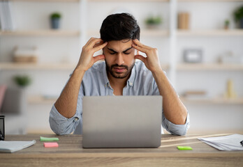 Deadline stress. Annoyed arab guy looking at laptop screen while sitting at workplace at home office