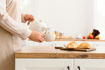 Woman pouring tea into cup near counter in kitchen