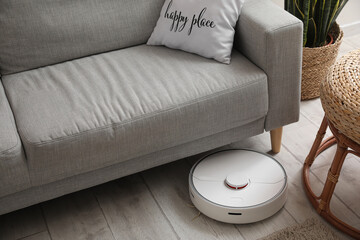 Modern robot vacuum cleaner near sofa in room