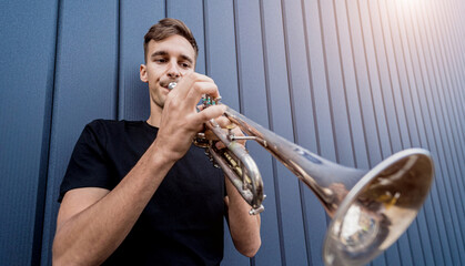 Young street musician playing the trumpet near the big blue wall © romaset