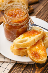 Glass jar of tasty pear jam and bread on table, closeup