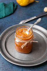 Plate with glass jar of tasty pear jam on dark background