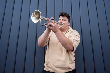 Young street musician playing the trumpet near the big blue wall