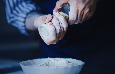 A cook in a blue apron and a striped shirt is holding a pepper mill in his hands, and seasoning...