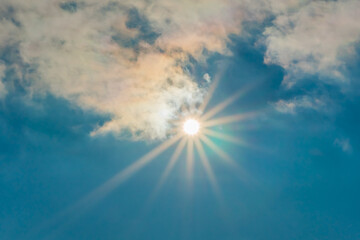 The sun in the blue sky under the clouds. Sunny day. Blue sky. Bright midday sun illuminates the...