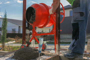 Improvement of the yard. A man pours concrete solution from an orange concrete mixer onto the...